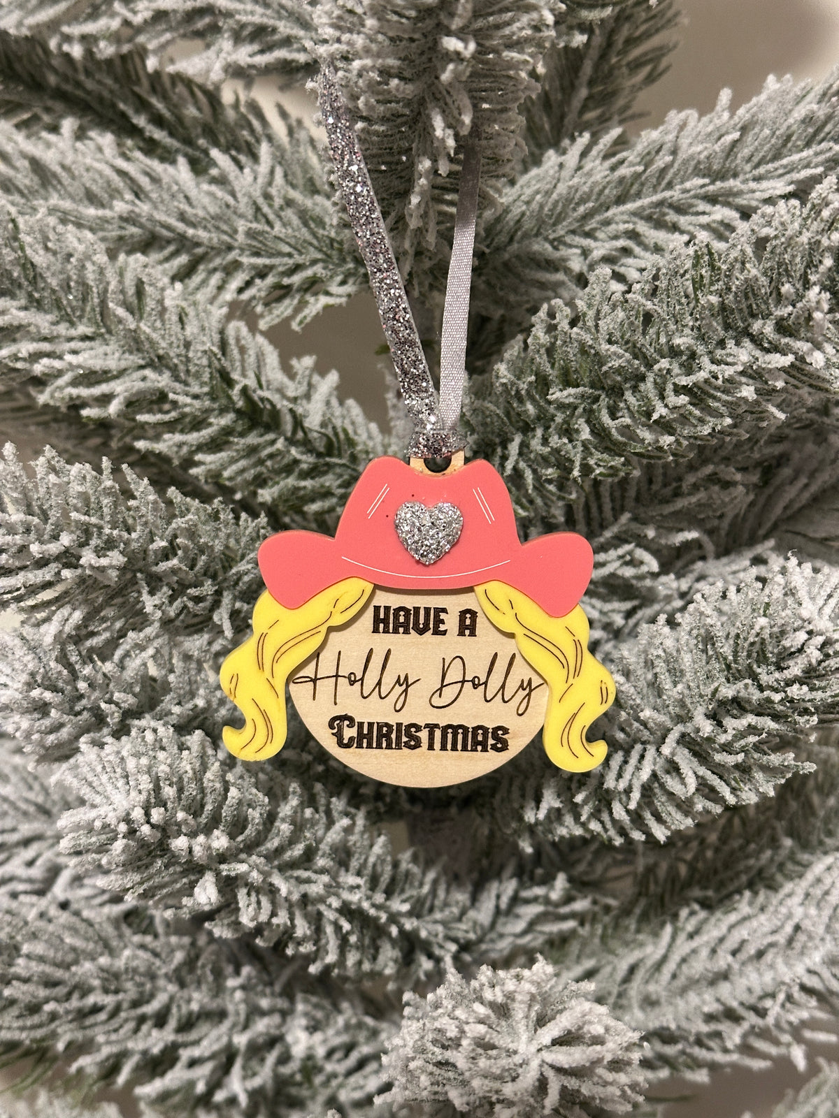 Wood and acrylic Christmas ornament featuring a pink cowgirl hat, blonde hair and the text have a holly Dolly Christmas.
