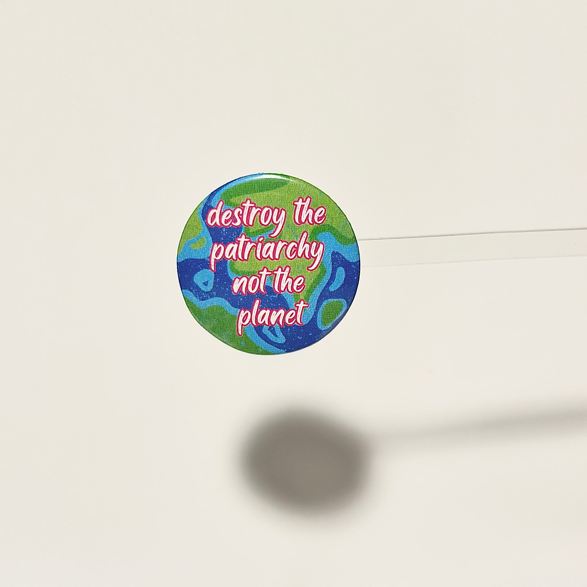 Button badge with 'destroy the patriarchy not the planet' text on a blue and green globe background