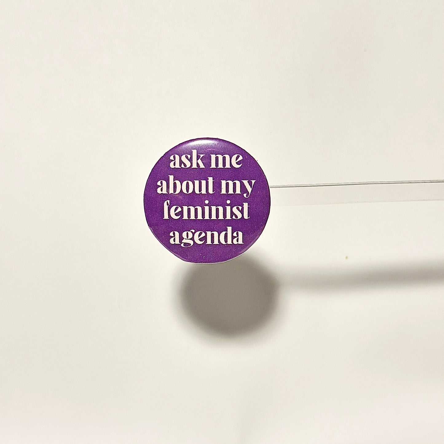 finback button with white text saying ask me about my feminist agenda on a purple background