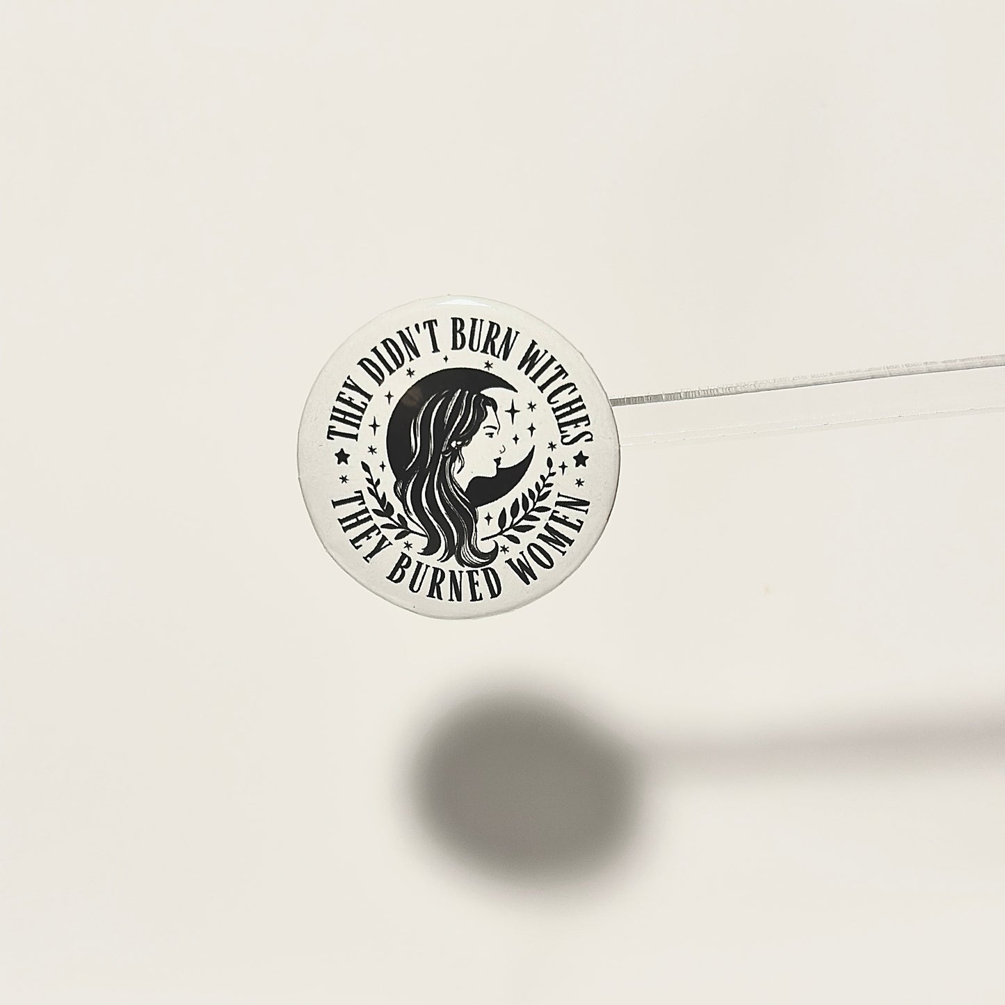 white pinback button with arched text saying they didn't burn witches they burned women. woman's head in profile with a crescent moon in center.